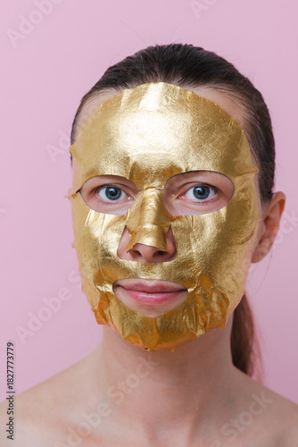 A woman with a golden facial mask against a pink background. The image represents self‑care, beauty and personal wellness. Vertical photo