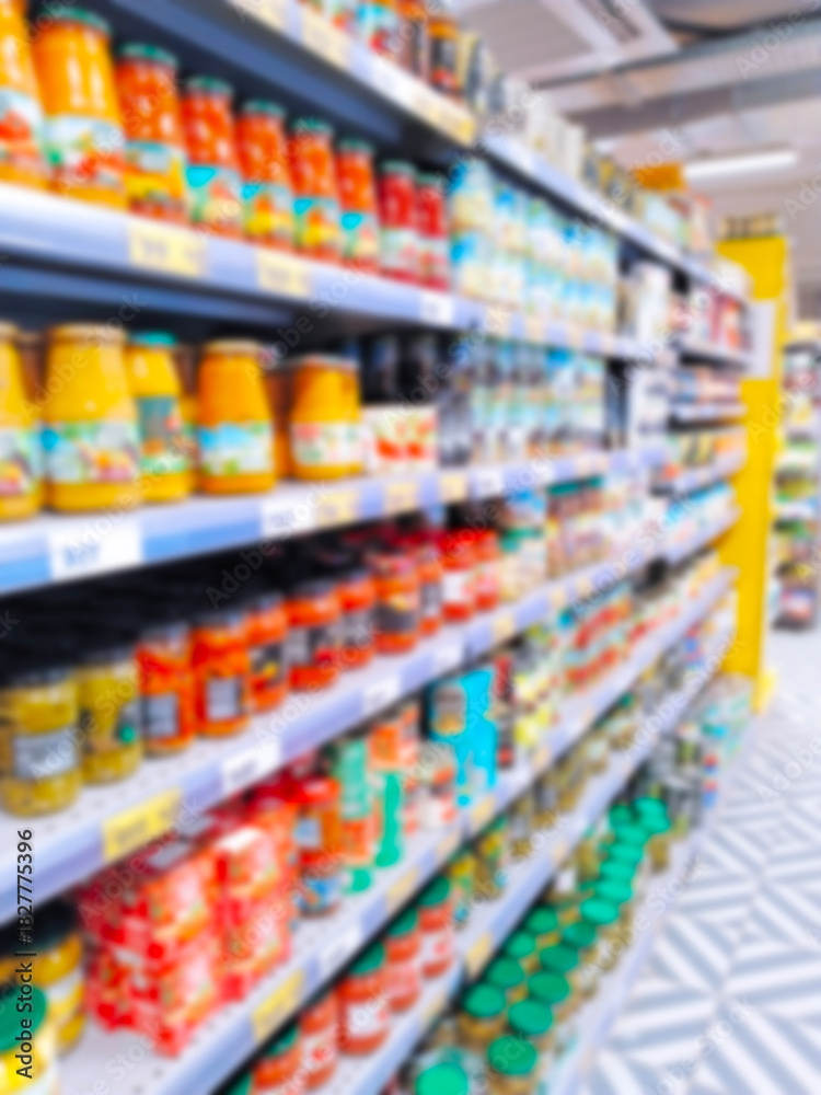 Fototapeta premium Blur supermarket background. Defocused shelves with products. Grocery store. Retail industry. Inflation concept. Aisle. Consumer packaged goods. CPG. Rack. Tariff. Price hikes. Jars of canned food.