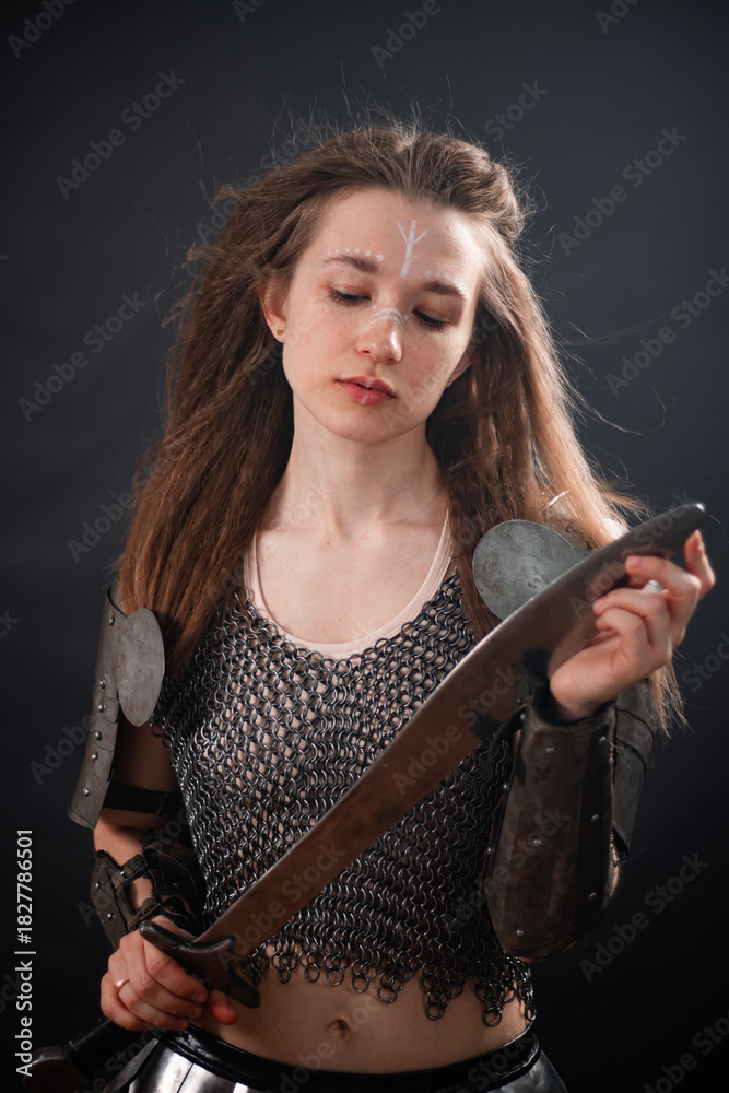 Obraz premium Portrait of a young woman, fantasy warrior in armor with a sword in her hands isolated on a dark background.