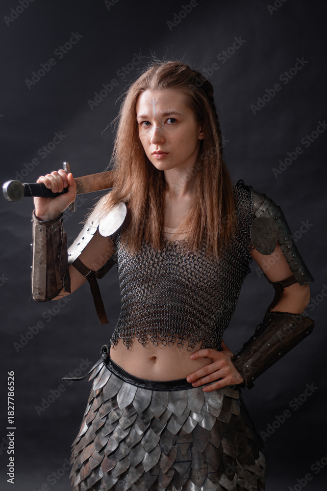 Naklejka premium Portrait of a young woman, fantasy warrior in armor with a sword in her hands isolated on a dark background.