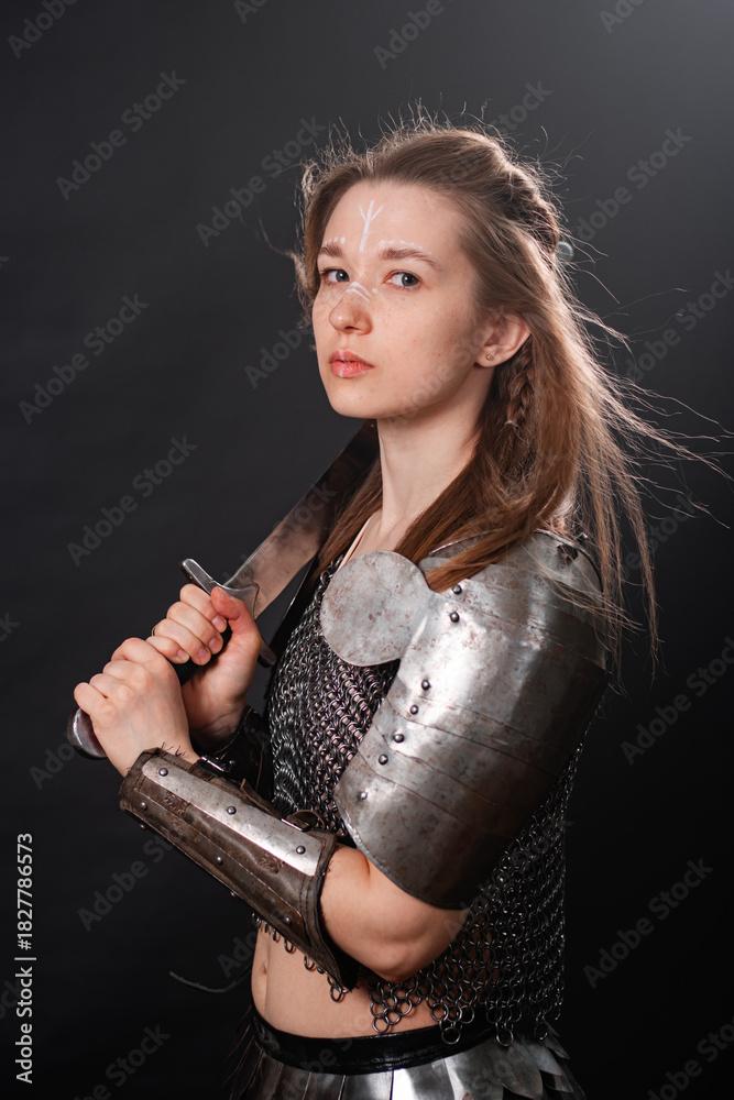 Obraz premium Portrait of a young woman, fantasy warrior in armor with a sword in her hands isolated on a dark background.