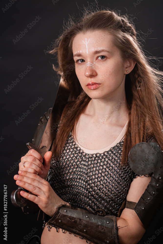Naklejka premium Portrait of a young woman, fantasy warrior in armor with a sword in her hands isolated on a dark background.
