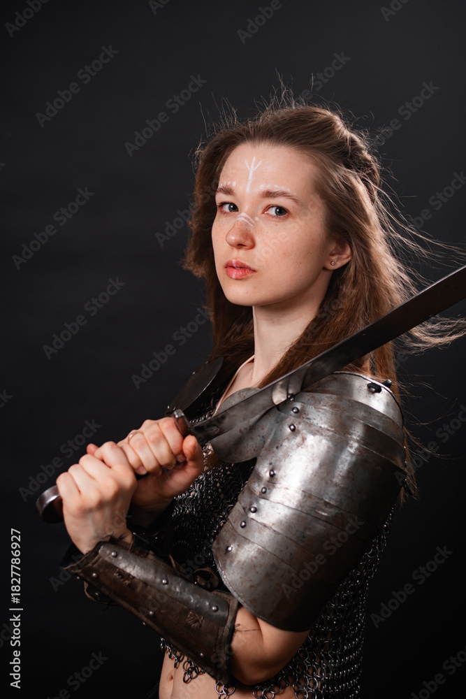 Naklejka premium Portrait of a young woman, fantasy warrior in armor with a sword in her hands isolated on a dark background.