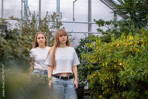 Mother and daughter standing together in a lush greenhouse, surrounded by vibrant greenery, showcasing their close relationship and shared moments of joy and connection