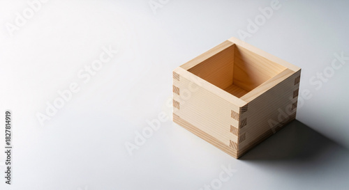 A traditional wooden sake cup, known as a masu, is isolated on white background