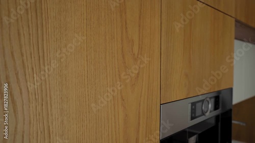 Smooth cinematic video of wooden kitchen facade texture with gentle camera movement transitioning to built-in stainless steel oven in modern minimalist interior