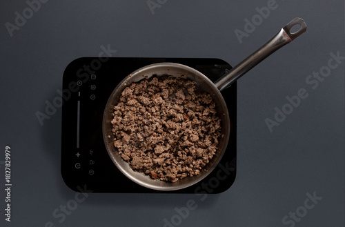 Ground meat browns in a stainless-steel pan on an electric stove. The kitchen setting is simple, focusing on the cooking process of the meat preparation.