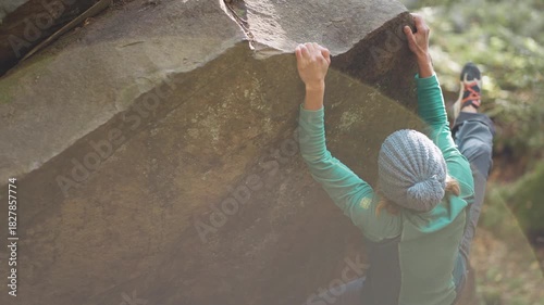 strong female climber climbs hard crag bouldering reaching holds on cliff edge showing strength and power of her fingers and forearms. healthy active leisure, rock climbing outdoors in autumn forest.