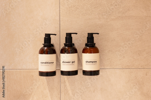 Brown bottle mockup for bathing products in hotel bathroom, spa shampoo, shower gel, liquid soap, body wash, and conditioner dispensers on shower wall.