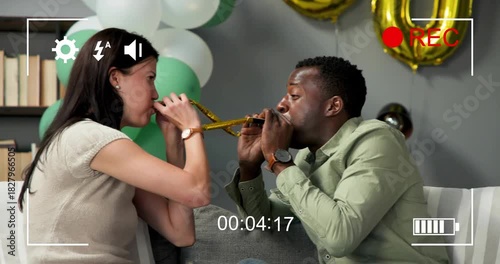 Couple exchanging gold blowers, testing and blowing on couch, celebrating with REC overlay, balloon