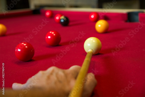A game of pool with selective focus on the tip of a pool cue as a player takes aim. 