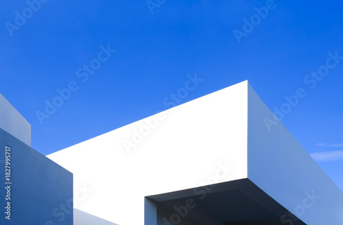 Minimal house exterior wall in modern design. Geometric concrete building with light and shadow on rooftop surface against blue sky background, low angle view with copy space