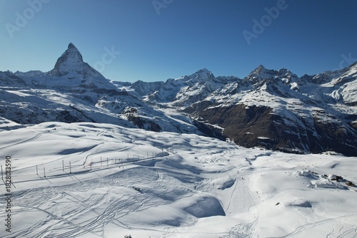 Aerial drone photo of the snowy Swiss Alps near the Matterhorn, showcasing wide glacier fields, winter terrain, and dramatic mountain scenery under a clear blue sky.