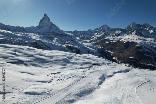 Aerial drone photo of the snowy Swiss Alps near the Matterhorn, showcasing wide glacier fields, winter terrain, and dramatic mountain scenery under a clear blue sky.