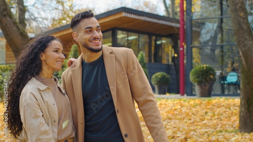 Hispanic happy couple in love outdoors talking in city fall season man and woman communicate in autumn park guy pointing away discuss talk with girl dating going away windy weather yellow foliage leaf
