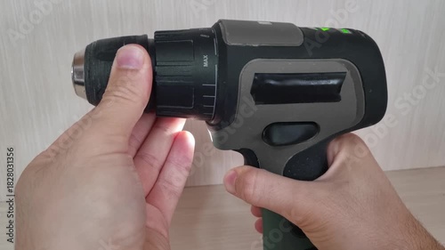 Close up detail of a hand manually rotating the keyless chuck of a cordless power drill counter-clockwise to loosen the jaws and remove a drill bit