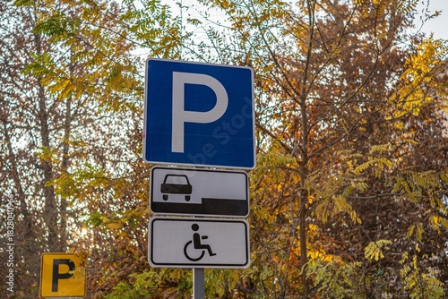 A parking sign indicating spaces for vehicles and accessible parking. Surrounded by autumn foliage, it highlights accessibility features.