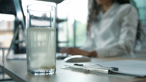 Close-up glass of still water business woman putting pill remedy painkiller inside at office unrecognizable businesswoman female girl worker ill sick manager with computer work preparing vitamin drink
