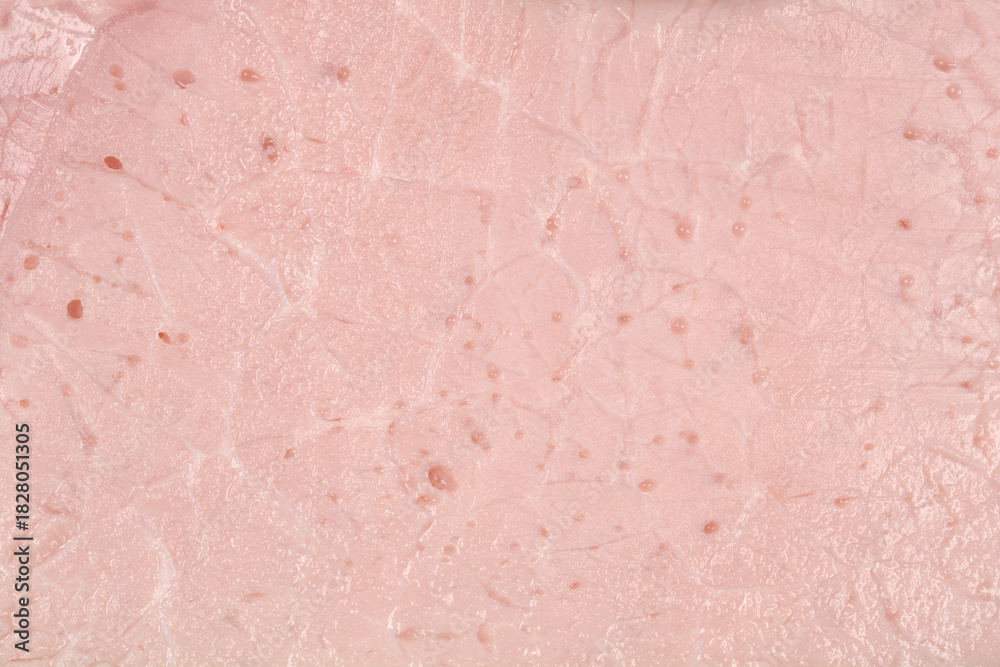 Fototapeta premium A macro close-up shot captures the smooth, processed texture and pale pink color of a thin slice of deli ham, showing small air pockets within the meat