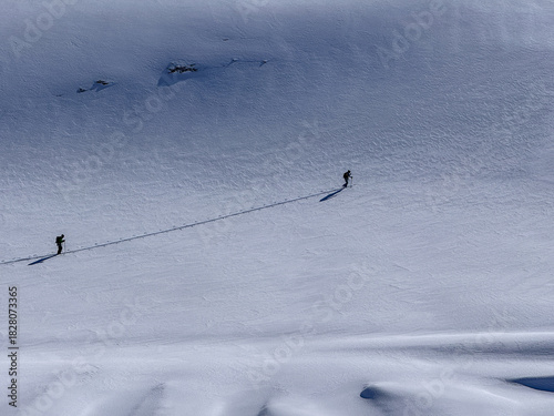 High-altitude snowy ridge with tiny skiers crossing an untouched alpine glacier under a deep blue sky. Serene winter landscape of the Swiss Alps.