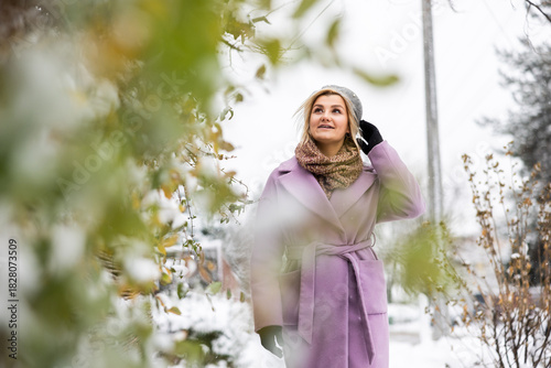 Winter stroll in a snowy garden with a woman wearing a purple coat and warm accessories enjoying the chilly weather