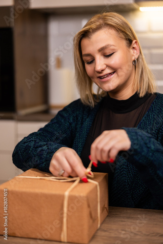Woman joyfully unwraps a gift at home in a cozy kitchen setting during the evening