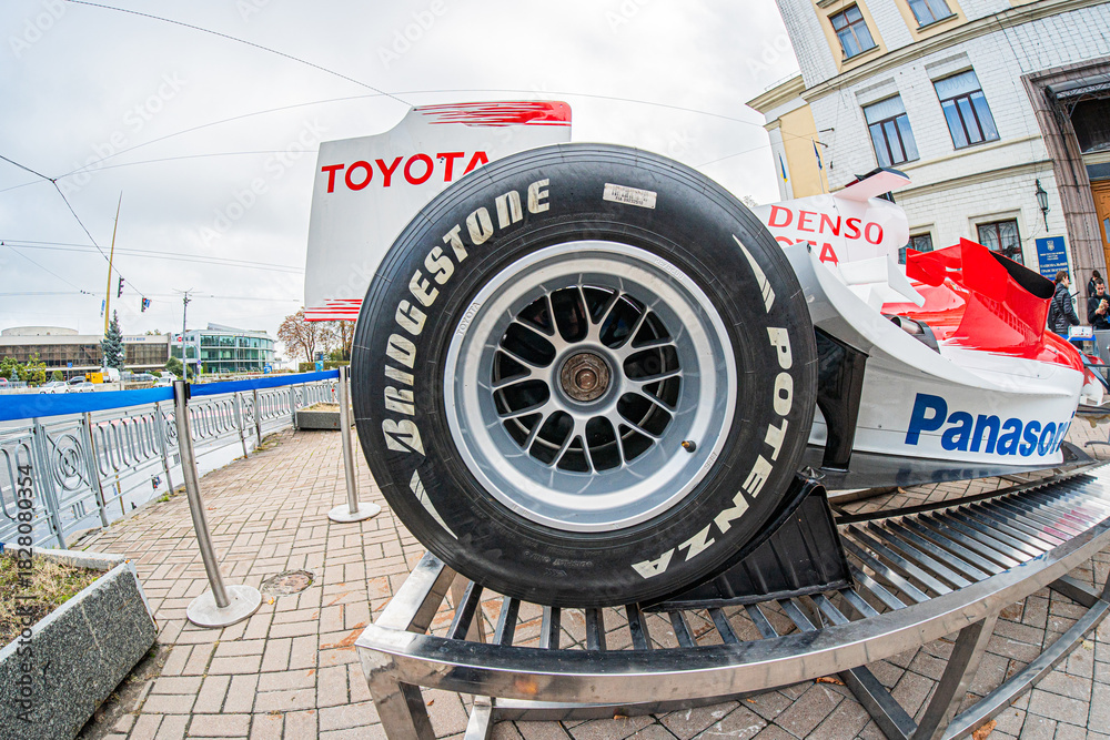 Obraz premium Formula 1 Toyota TF-108 car on wheel stand, primarily red and white with sponsor logos Aerodynamic design, outdoor setting near a race track, natural lighting with - Kyiv, Ukraine 10-10-2024