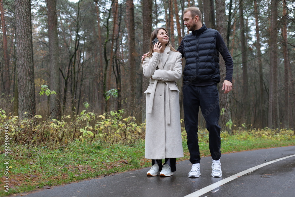 Fototapeta premium Couple enjoying an autumn walk in the forest, woman on a phone call