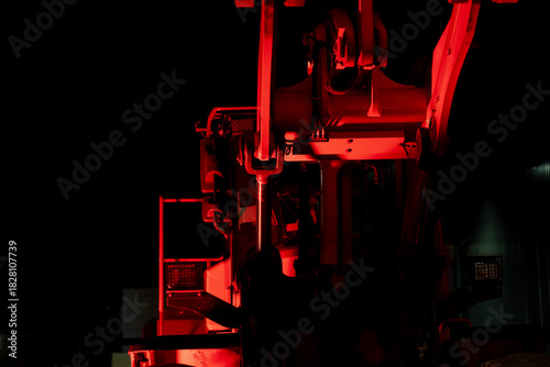 Front-facing perspective of an industrial hydraulic machine showing pistons, arms, and mechanical structures strongly lit by red lighting within a low-visibility technical or industrial setting