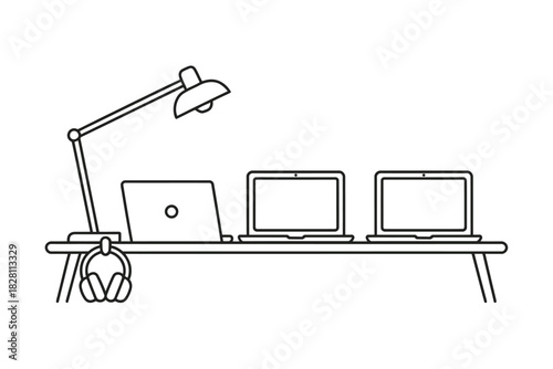 A modern desk setup features three laptops and a desk lamp illuminating the workspace.