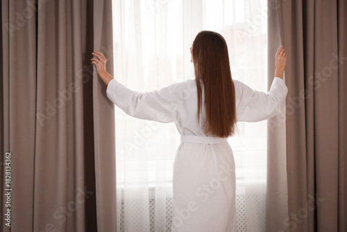 Free Download Woman in white bathrobe opening curtains indoors, back view - GFXLoad