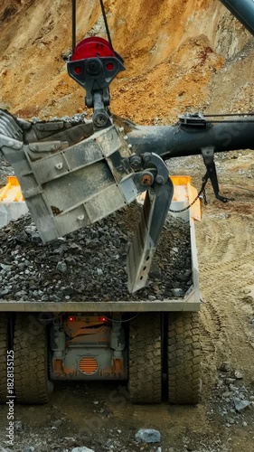 heavy material tipping into bed, crushed stone being unloaded onto vehicle with overcast weather overhead