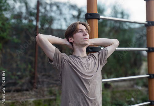 A young man with his hands folded behind his head, against the backdrop of a sports ground