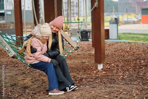 Mother and child sitting together on swing at playground