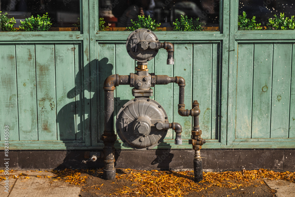 Fototapeta premium Outdoor natural gas meter and pipeline system mounted on a wooden wall in Toronto, Canada. Industrial metal pipes, shutoff valves and distribution unit in autumn daylight.