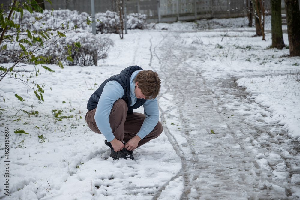 Fototapeta premium Man tying shoes in snowy winter park. Outdoor Lifestyle