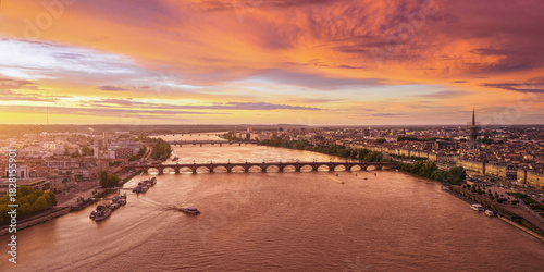 Aerial view of the Garonne River reflecting the fiery sunset, flowing under the Pont de Pierre towards the cityscape, Bordeaux, Nouvelle-Aquitaine, France.