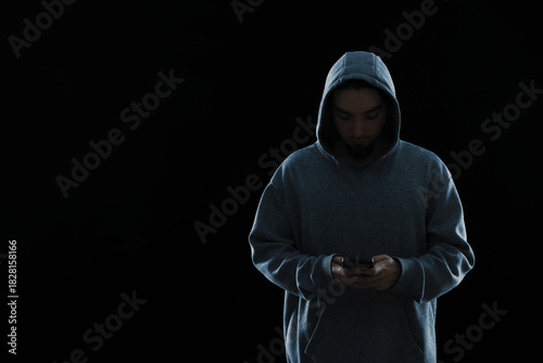 Obraz na plátně Criminal in hood with smartphone on black background, space for text
