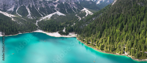 Aerial view of shimmering turquoise waters meet the rugged, snow-dusted mountains and dense evergreen forests, creating a stunning contrast, Dobbiaco, Trentino-Alto Adige, Italy.