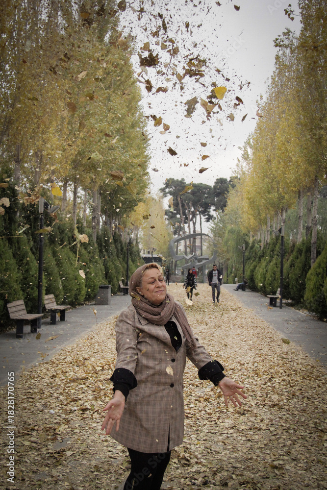 Fototapeta premium A woman throws autumn leaves into the air in a park in Tehran, the capital of Iran