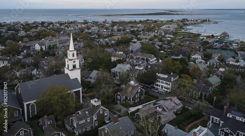 Aerial view of the First Congregational Church steeple rising above the quaint rooftops of a historic town nestled by the calm ocean, Nantucket, Massachusetts, United States.
