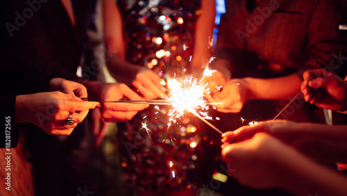 Hands hold sparklers, creating bright sparks in a lively setting. Friends celebrate together as lights twinkle and laughter fills the air during a special event.