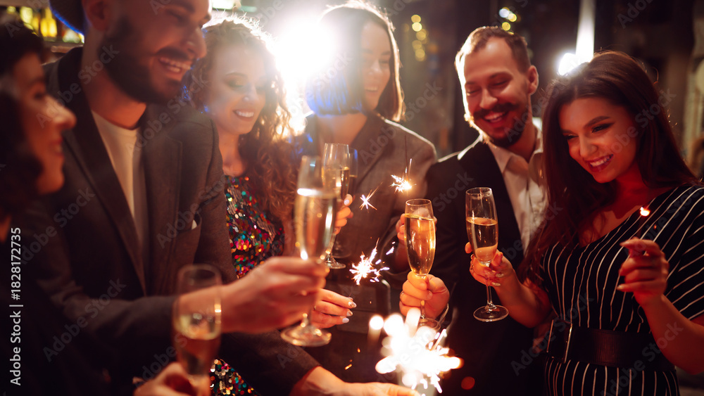 Obraz premium Friends gather at a vibrant bar to celebrate New Year's Eve. They enjoy drinks while holding sparklers, surrounded by a festive atmosphere and sparkling decorations.