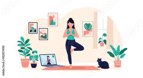 Woman practicing yoga in a tree pose at home while following an online fitness class on her laptop with her cat watching.