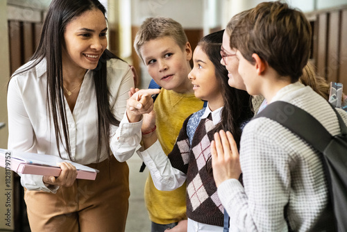 The teacher walks through the school lobby while talking with her students as class is about to begin. The moment feels relaxed and friendly, with everyone easing into the school day.