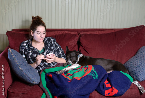 Young woman relaxing on a sofa, looking at her cell phone, with her sleeping dog