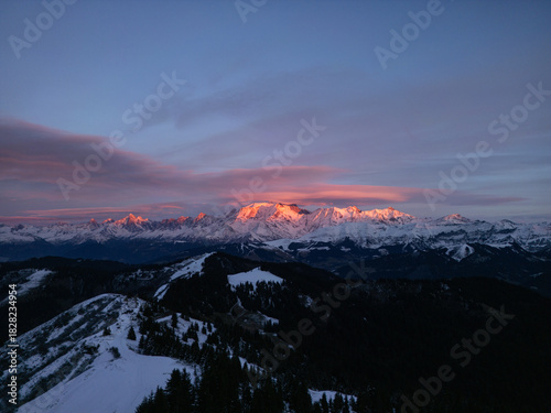 Aerial view of the snow-capped peaks ablaze with the fiery hues of dawn, casting long shadows over the pristine, untouched landscape, Megeve, Auvergne-Rhone-Alpes, France.