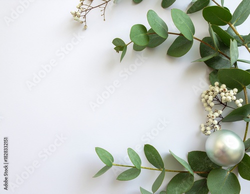 A delicate frame of eucalyptus leaves and baby's breath accented with a silver bauble on a white background, evoking a sense of natural elegance and festive cheer