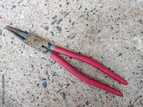 Old rusty snap ring pliers with red handles isolated on concrete texture