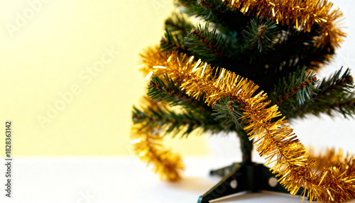 Small artificial Christmas tree wrapped in gold tinsel against a simple two-tone background.